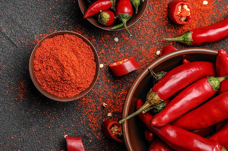 Red hot peppers next to chile powder in a bowl