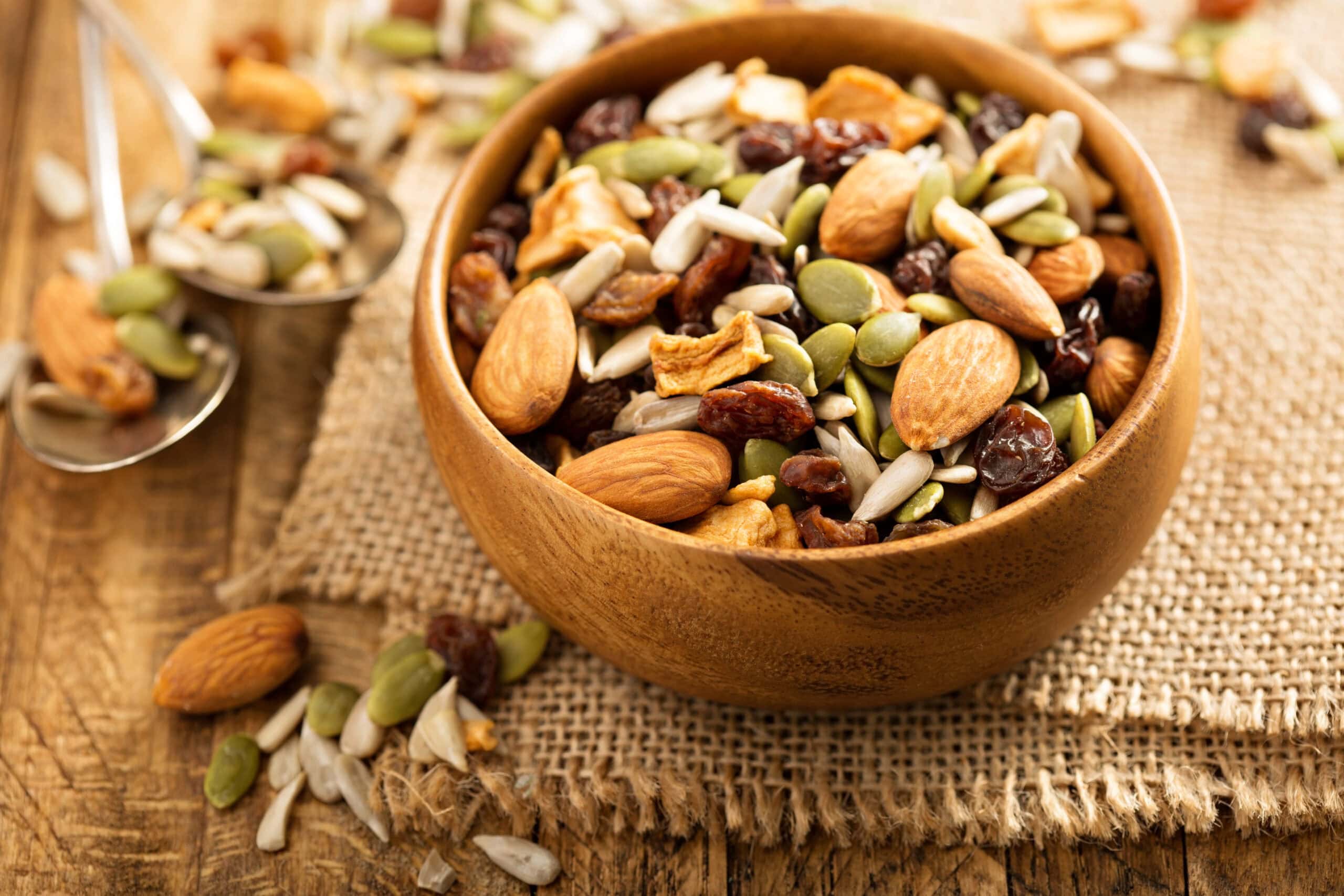 Dried fruit and nuts trail mix with almonds, raisins, seeds and apples in a wooden bowl