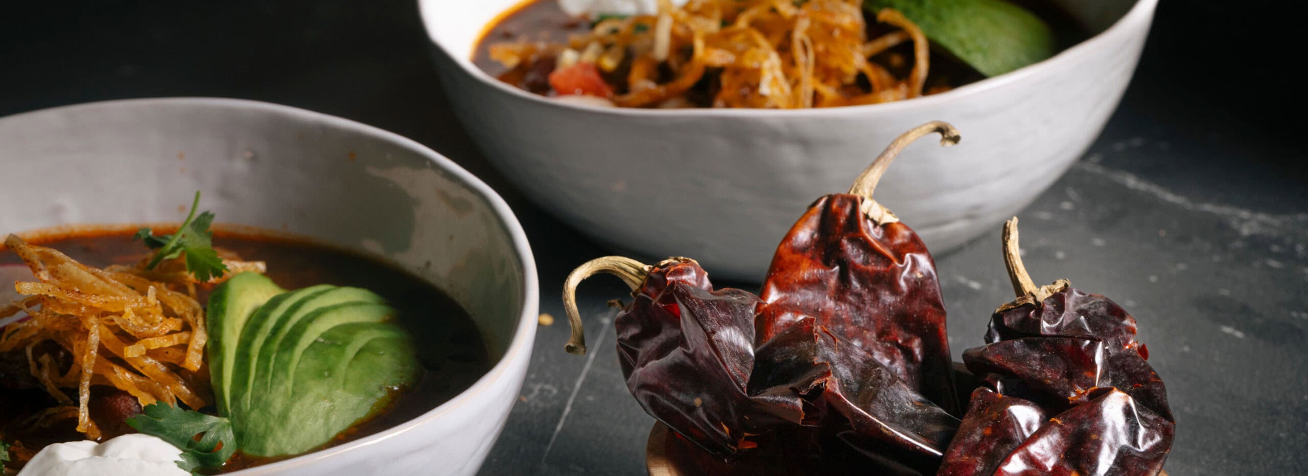 Dried red chiles on a table with two bowls of colorful soup