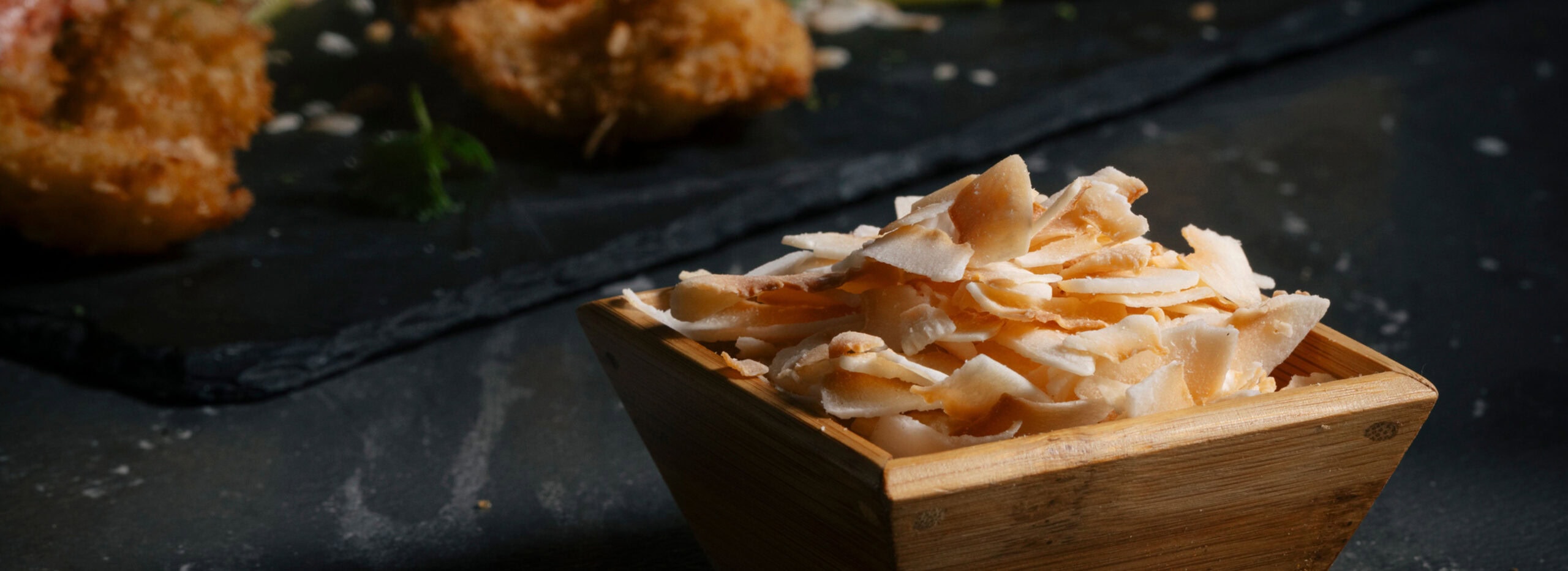 Coconut in a wooden bowl in front of coconut dried shrimp.