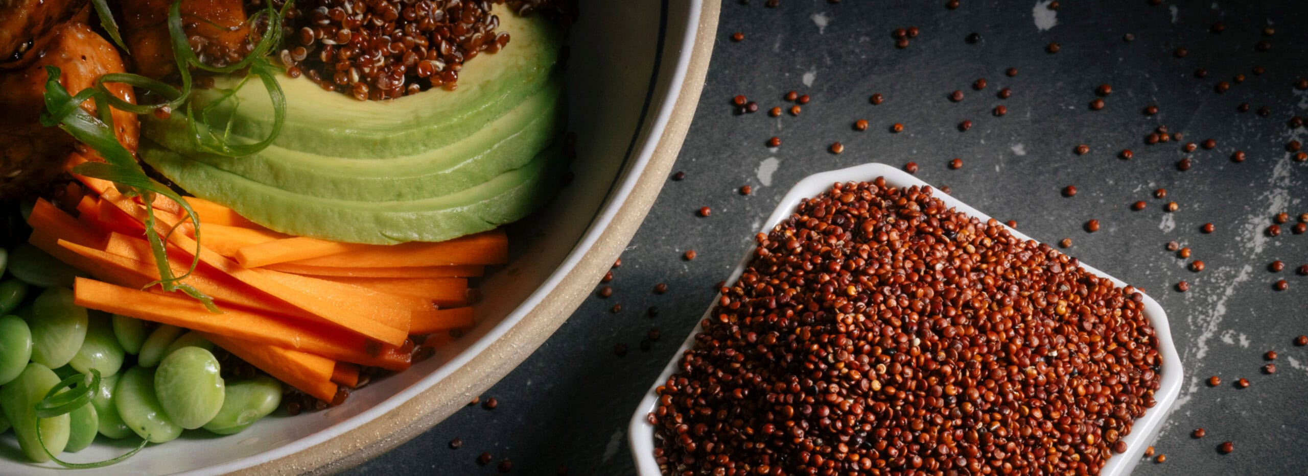 Ancient grains in a bowl on a gray table next to a rich, colorful salad