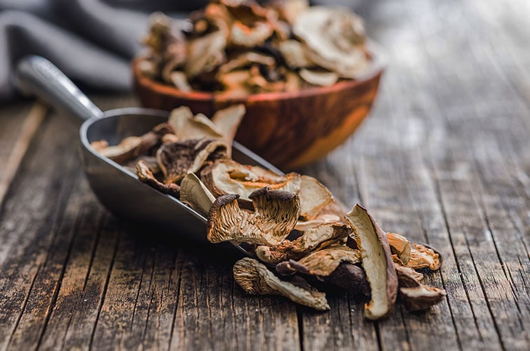 a scooper and a wooden bowl with dried mushrooms